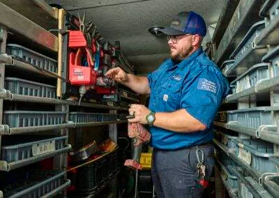 A technician in a blue uniform organizing tools in a van with shelving units